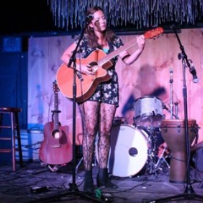 Picture of Irene Molloy carrying a guitar during a stage performance.